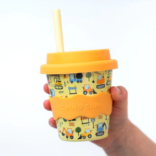 Yellow tumbler with construction vehicle pattern and orange lid held by a hand on a white background